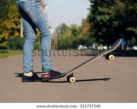 Feet in sneakers on a skateboard. Park, summer. Torn jeans. Road