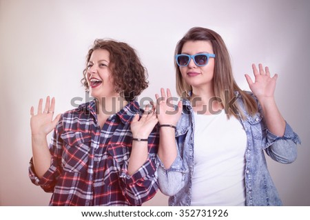 Two young girl friends standing together and having fun. Showing signs with hands. Looking at camera