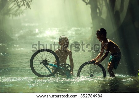 The boys playing with bicycle water splash on creek,Nhongkhai,Thailand. Royalty-Free Stock Photo #352784984