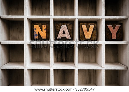 The word "NAVY" written in vintage ink stained wooden letterpress type in a partitioned printer's drawer.