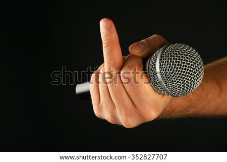 Male hand holding microphone with finger insult ignore gesture on black background