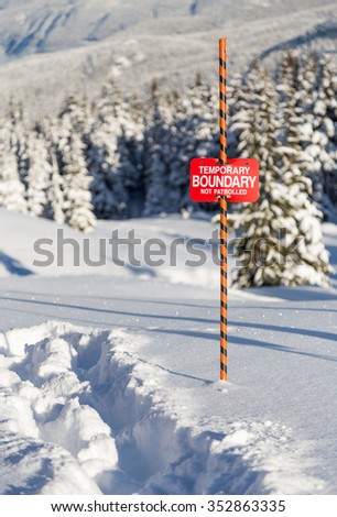 Tracks in the snow beside a ski area boundary sign. 