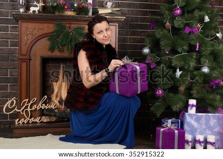 beautiful woman in a blue evening dress posing near the Christmas tree with the words Happy New Year in russian language in the background