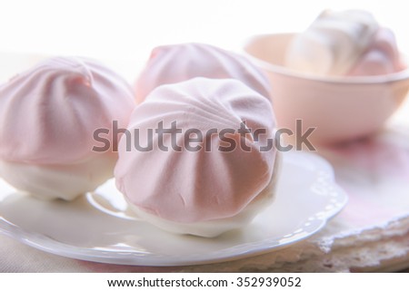 Still life in pastel colors with pink and white marshmallows on a white plate with a napkin
