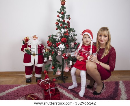 Happy New Year concept. Merry girl in red dress and hat of Santa Claus with Christmas tree.