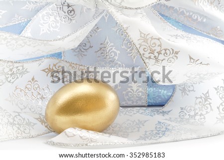 Ice blue wrapped package with silver and white ribbon placed behind gold nest egg.  Concept image reflects gift of start or addition to portfolio or savings, a wise holiday gift.  