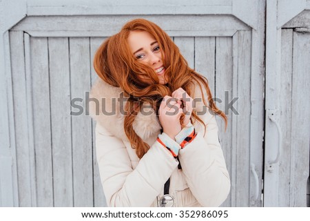 Portrait of a beautiful red hair young woman in warm clothes outdoor on the grey wooden background. Girl shows different emotions.