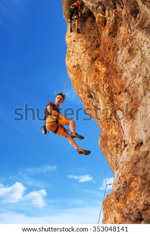 Adult male rock climber hanging on belay rope against the blue sky and mountains - stock image