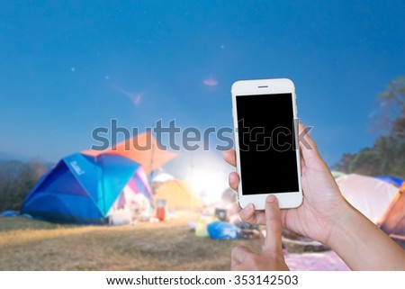 Hands woman are holding touch screen smart phone,tablet on blurred 
camp in forest at night holiday  background.