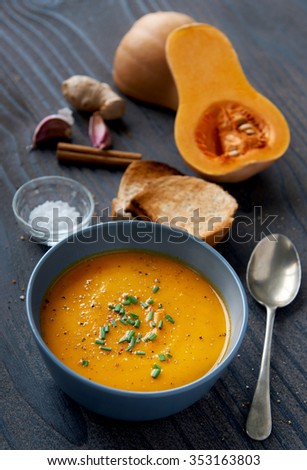 Bowl of butternut soup garnished with chives, raw ingredients in the background