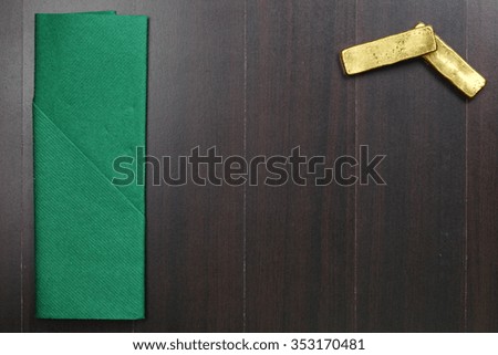 The green color fabric napkin on the dark color wooden dining table floor and gold bar represent the cleaning material and business concept related idea.