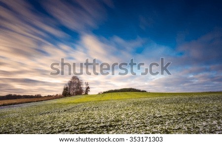 Early winter or late autumnal landscape of long exposure field at good weather. Fields with little snow.