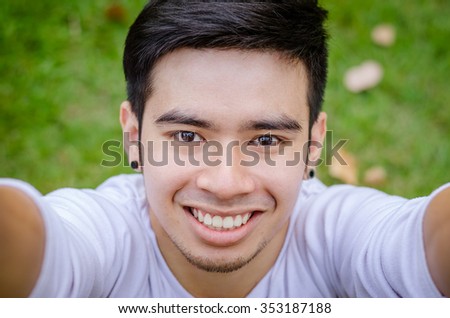 Portrait of a smiling young asian man making selfie photo in park