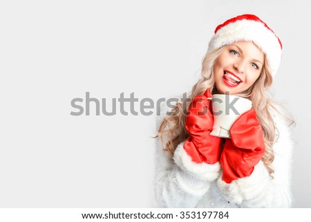 Christmas girl drinking tea to keep warm in winter. Santa hat isolated portrait of a woman on a gray background.
