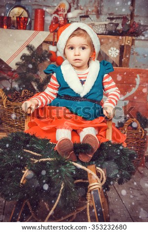 Girl in suit of Christmas elf sitting in a sled