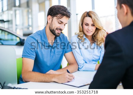 Photo of young male consultant and couple. Young woman and man buying new car in auto show. Signing of contract. Concept for car rental