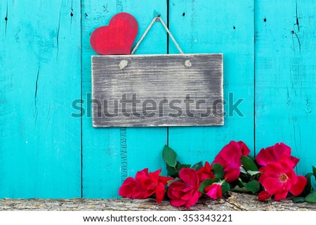 Blank sign with red heart by red roses on log border hanging on antique teal blue rustic wooden background; Valentines Day, Mothers Day and love concept background with painted wood copy space