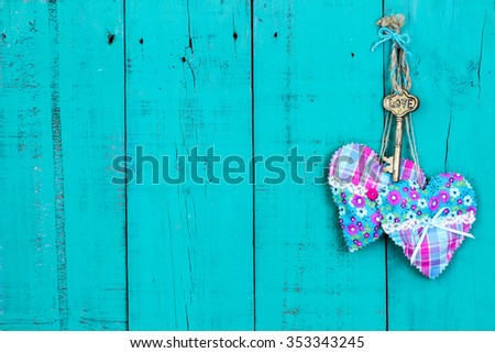 Brass skeleton key and pink and turquoise fabric hearts hanging on antique rustic teal blue wooden door 
