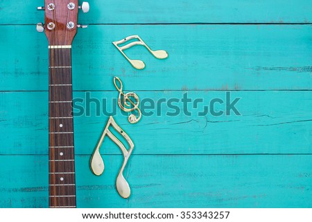 Gold musical notes by neck of guitar with antique rustic teal blue wooden background