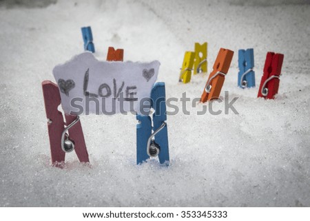 stock photo of small colorful wooden clothes pins placed side by side on snow holding paper that says love 