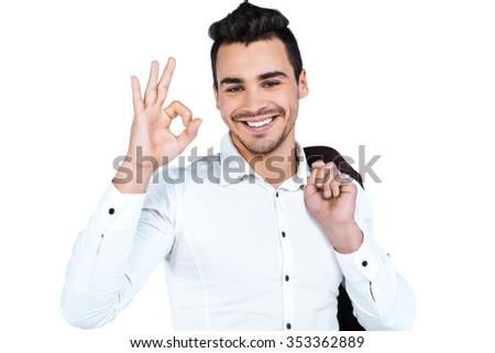 Portrait of young businessman standing on white background, smiling, showing ok sign and looking at camera