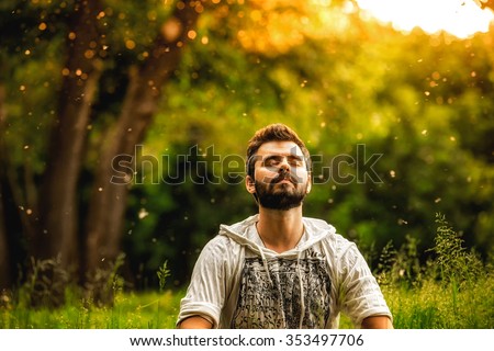 A bearded man is meditating on green grass in the park with face raised up to sky and eyes closed on sunny summer day. Concept of meditation, dreaming, wellbeing and healthy lifestyle Royalty-Free Stock Photo #353497706
