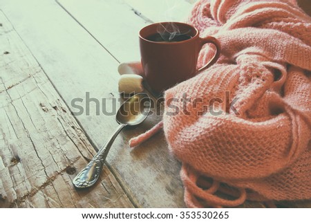 selective focus photo of pink cozy knitted scarf with to cup of coffee on a wooden table. workspace or coffee break. retro filtered