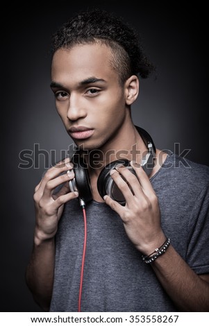 Keep calm and listen good music. Young African man adjusting headphones and looking at camera while standing against black background