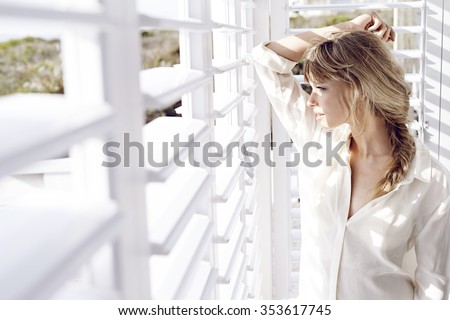 Sunlight on stunning young lady looking though shutters Royalty-Free Stock Photo #353617745