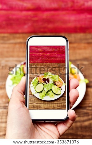 closeup of a young caucasian man taking a picture with his smartphone of a plate with salad placed on a wooden table