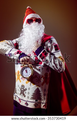 Picture of funny Santa Claus with alarm clock wearing heart shape sunglasses on bright festive bokeh background