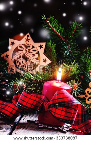 Christmas composition with burning red candles tied with plaid ribbon with a bow, snowflakes, pine cones and spruce branches, dark toned image, selective focus