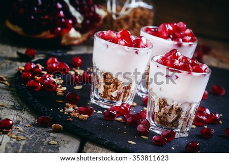 Breakfast with baked muesli, yoghurt and pomegranate, portioned in glasses on a dark background, selective focus