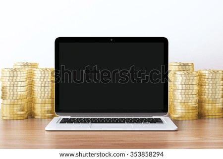 Blank black screen of laptop with pile of gold coins on wooden table, mock  up