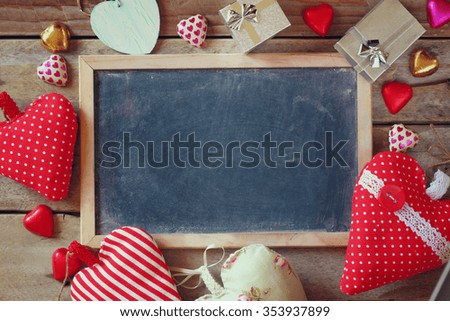 top view image of colorful heart shape chocolates, fabric hearts, gift boxes and chalk board on wooden table. valentine's day celebration concept
