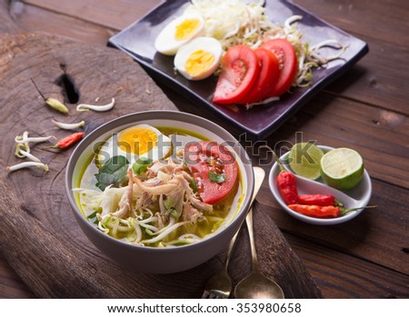 Soto: Indonesian chicken soup with hard boiled eggs, tomato, bean sprout, lemon, cayenne pepper on rustic brown wooden background