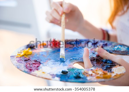 Closeup of paintbrush in woman hands mixing paints on palette Royalty-Free Stock Photo #354005378