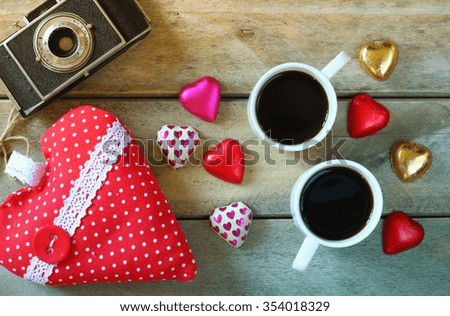 top view image of colorful heart shape chocolates, fabric heart, vintage photo camera and cup of coffee on wooden table. valentine's day celebration concept. retro filtered and toned
