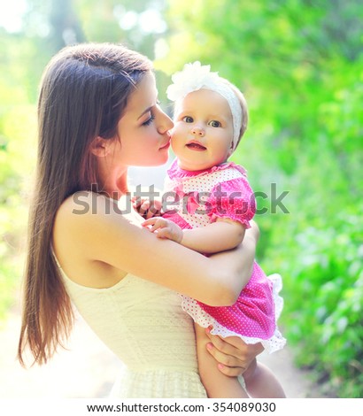 Happy mother hugging and kissing baby in summer day