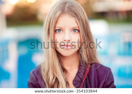 Beautiful blonde teenage girl 13-15 year old posing outdoors over blue. Looking at camera.  Royalty-Free Stock Photo #354103844