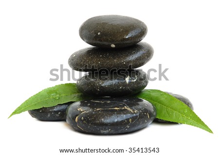 Stack of black stones for hot stones spa treatment and green leaves on white background