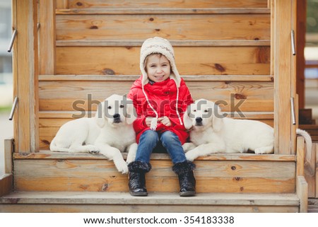 portrait of Beautiful girl with her two dogs labrador retriever. little child with two puppies of golden retriever sitting on stair steps. outdoor. cold weather. happy child