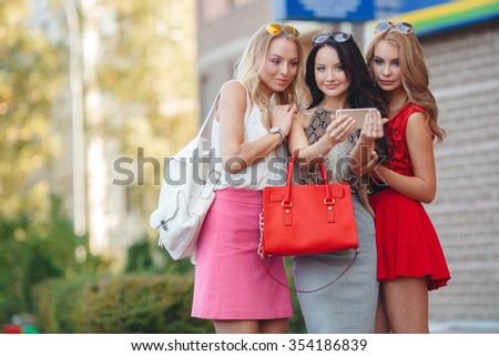 Three young beautiful russin women making self portrait outdoor in the city. Girls making selfie. Friends. Portrait of a three smiling girlfriends making selfie photo on smartphone in the street