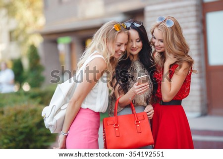 three young beautiful girls friends having fun in the city street. A picture of three friends using smartphone in the city. three beautiful friends. fashion look