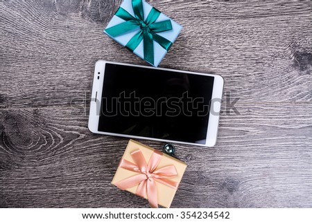 Tablet computer with blank black screen among christmas gifts on wooden background. Holiday image for New Year and Christmas. Vintage texture for design uses. Banner template for web ads.