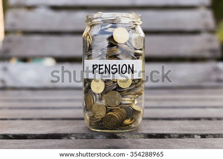 Coins in the jar or glass on the wood with PENSION label against bokeh background. Financial concept. Selective focus.