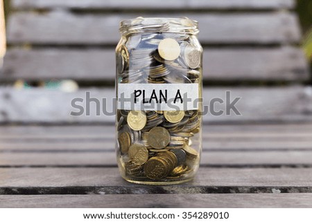 Coins in the jar or glass on the wood with PLAN A label against bokeh background. Financial concept. Selective focus.