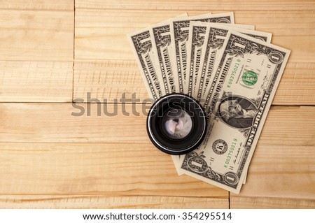 Photo lens with money on light wooden background. Buying expensive photographic equipment.