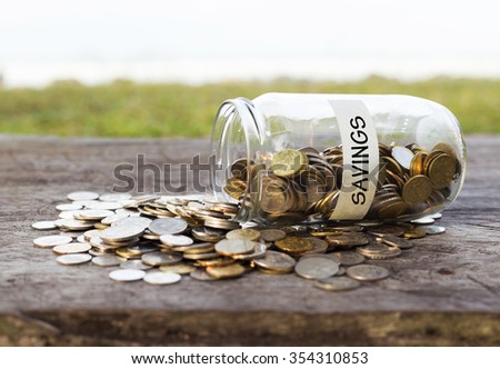 Coins in the jar or glass on the wood with SAVINGS label against bokeh beach background. Financial concept. Selective focus.