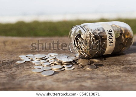 Coins in the jar or glass on the wood with HOME label against bokeh beach background. Financial concept. Selective focus.